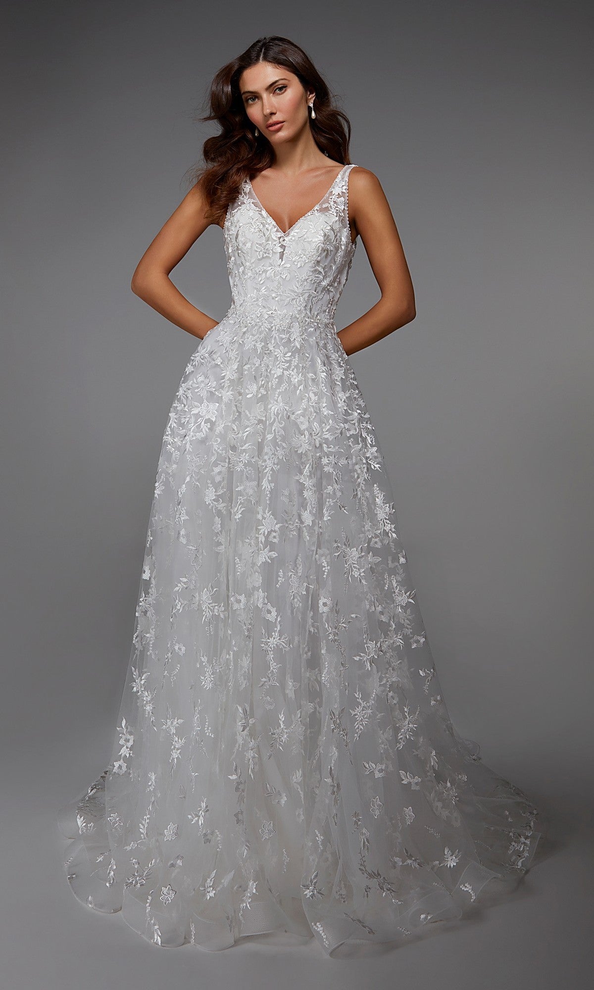 A woman models the Alyce 7037 long ivory dress featuring a sleeveless design, V-neckline, and floral lace details, set against a plain grey background.
